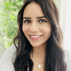 photo of Violeta Murrieta smiling with long dark hair, dark eyes, a silver necklace and white and green blouse with green leafy background